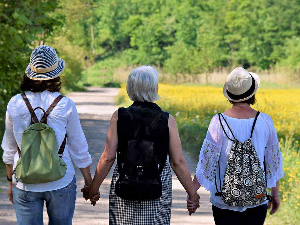 Drei Frauen spazieren Hand in Hand durchs Grüne.